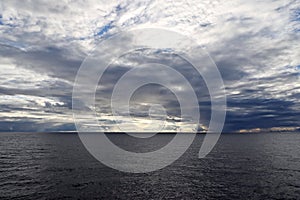 The clouds are multicolored, thunderous bizarre shapes against the blue sky and the sun above the ocean surface. Seascapes.