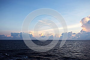 The clouds are multicolored, thunderous bizarre shapes against the blue sky and the sun above the ocean surface. Seascapes.