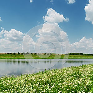 Clouds over river and meadow with chamomiles