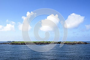 Clouds over small island on bright sunny day in Ireland. White fluffy clouds in line over small isle.