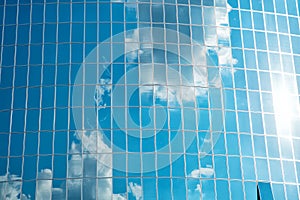 Clouds reflected on glass facade wall of building. Cloudy blue sky reflection in windows. Modern glass architecture