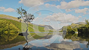 Clouds reflecting on lakes surface with beautiful british landscape reflections of lone tree and cl