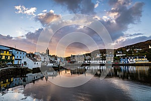 Clouds start to turn pink reflecting in the still water of Tarbert Harbour with the painted houses on Barmore Rd Scotland