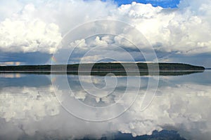 Clouds white on blue sky with a small rainbow with reflection in lake during the day in the natural environtent.