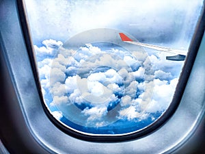 Clouds and a wing through a porthole in an airplane. Aerial View of Fluffy Clouds and Airplane Wing From Cabin Window