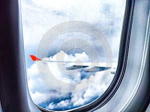 Clouds and a wing through a porthole in an airplane. Aerial View of Fluffy Clouds and Airplane Wing From Cabin Window