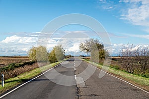 Cloudy country repaired highway/road in bad condition and blue cloudy sky. Green and yellow/orange fields, sunny landscape