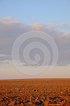 Cloudy evening sky over an empty agricultural field. Bright sunset landscape