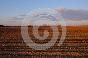 Cloudy evening sky over an empty agricultural field. Bright sunset landscape