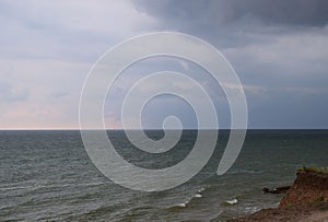 A cloudy grey sky shrouds the white foamy tipped teal waters of this beach