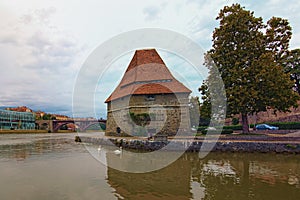 Cloudy landscape of Drava River in Maribor. The ancient Water Tower and Old Bridge at the background. Vibrant cloudy sky.