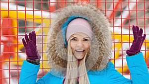 Cloudy outdoor winter portrait of young happy adorable woman in bright cyan coat posing in winter city park against bright red and