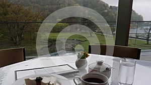 Cloudy rainy morning outside the window. Breakfast table at the window facing the mountains, pond and lake