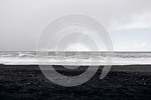 Cloudy skies, Atlantic Ocean waves and black sand on Vik beach, Iceland.