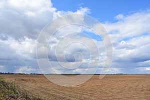 Cloudy sky in bright blue. Thick cloud. Agricultural field. A large ploughed field is boundless