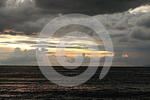 A cloudy sky over the ocean with a dark sky and the sun setting behind it