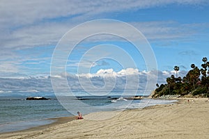 Cloudy sky over one person near the ocean and on a sandy beach