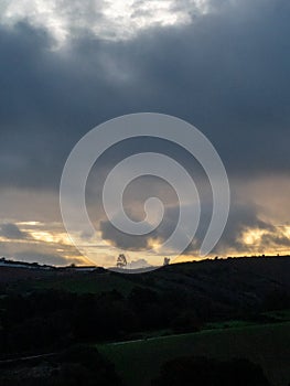 Cloudy sunrise over a countryside silhouette.