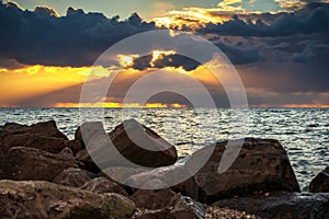 Cloudy sunset over a lake with rainy dark storm clouds and sunbeams and sun harps