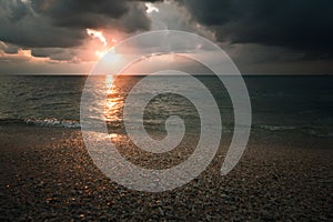 cloudy sunset over the sea in a rocky beach with stones and red dusk