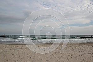 Cloudy weather. Golden sand, waves and foam. Cloudy day on the sandy beach. Panoramic view of beautiful sandy beach