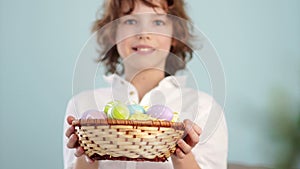 Clouse up ap portrait of a curly red-haired boy with a basket of Easter eggs in his hands. Happy easter