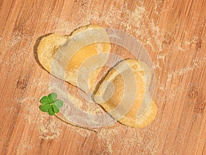 Clover with two raw handmade ravioli in the shape of heart,covered with flour and placed on the wooden table.