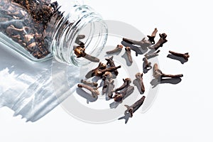 cloves are scattered from a glass jar. spice on white