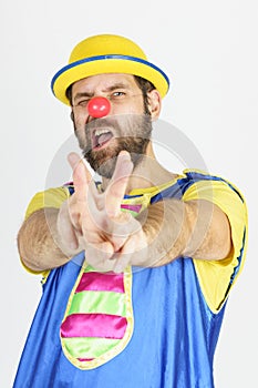 A clown in a bright blue and yellow suit shows a slingshot with his hands - aims