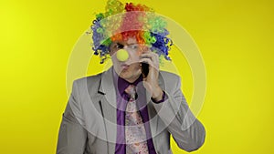 Clown businessman entrepreneur boss talking on mobile phone. Yellow background