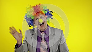 Clown businessman entrepreneur boss in wig waves his hands. Yellow background