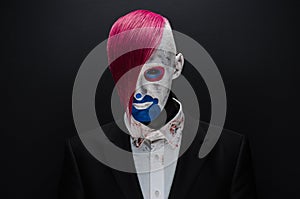 Clown and Halloween theme: Scary clown with pink hair in a black jacket with candy in hand on a dark background in the studio