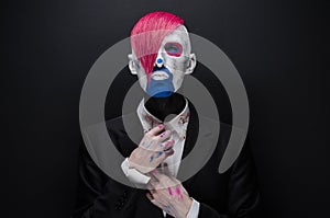 Clown and Halloween theme: Scary clown with pink hair in a black jacket with candy in hand on a dark background in the studio