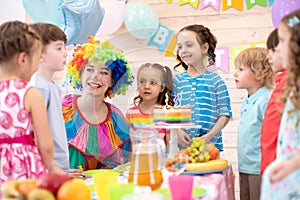 Clown playing with children. Kids group celebrate birthday at table. Holiday in a children`s club.