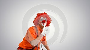 Clown prowling and making be quiet gesture to camera on gradient