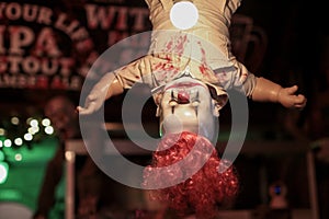 Clown with red hairs hanging upside down on ceiling with light on body