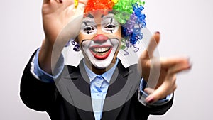 Clown woman in business suit and colorful wig making gun signs from hands