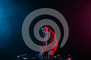 Club DJ mixing vinyl records with sound mixer on a party in night club. Young adult male person performing as a disc jockey