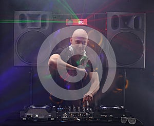 Club DJ with white headphones playing music and dancing at party lens flare from nightlife lights. Loudspeakers and lasers on back