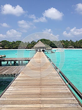 Club Med Kani, long pier surrounded by emerald sea, with huts in distance. photo