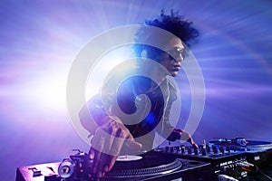 El Club de DJ con estilo de peinado afro de juego que mezcla la música en giradiscos de vinilo en la parte que usar gafas de sol con la llamarada de la lente de la vida nocturna de las luces.