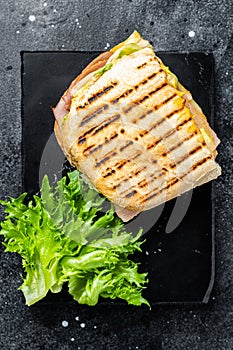 Club sandwich panini with ham, tomato, cheese and basil. Black background. top view