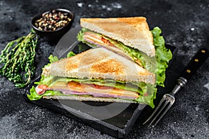 Club sandwiches with pork ham, cheese, tomatoes and lettuce on a wooden cutting board. Black background. Top view