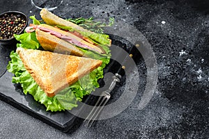 Club sandwiches with pork ham, cheese, tomatoes and lettuce on a wooden cutting board. Black background. Top view. Copy
