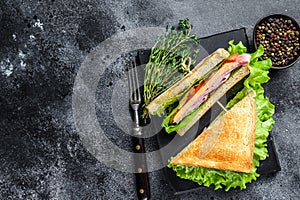 Club sandwiches with pork ham, cheese, tomatoes and lettuce on a wooden cutting board. Black background. Top view. Copy