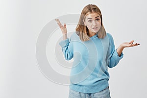 Clueless girl dressed in sweater and jeans shrugging shoulders, staring at camera with confused look after she did