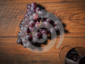 Cluster of juicy red grapes on a dark wooden table and a glass of red wine