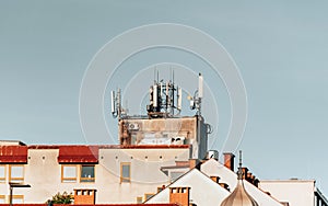 Cluster of mobile network broadcast cell repeaters on roof of building in city.