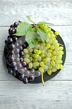 A cluster of white and red grapes on a round straw tray and grey wooden table