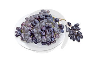 Clusters of blue grapes on a white dish and beside